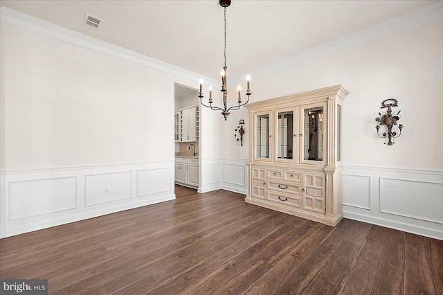 unfurnished dining area featuring an inviting chandelier, dark hardwood / wood-style floors, sink, and crown molding