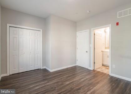 unfurnished bedroom with a closet, dark wood-type flooring, and ensuite bath