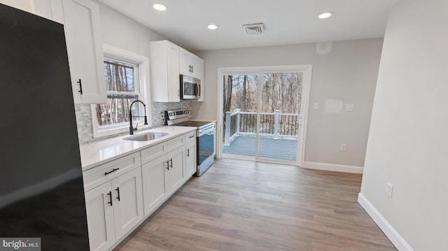 kitchen with backsplash, sink, light hardwood / wood-style floors, white cabinetry, and stainless steel appliances