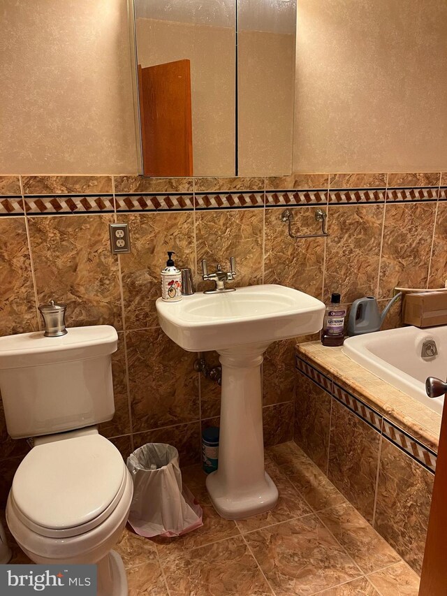 bathroom with a bathtub, sink, tile walls, tile patterned flooring, and toilet