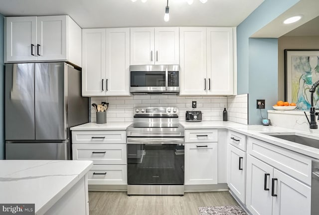 kitchen featuring decorative backsplash, light hardwood / wood-style flooring, appliances with stainless steel finishes, white cabinets, and light stone counters