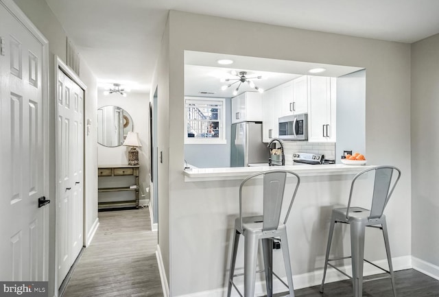 kitchen featuring appliances with stainless steel finishes, white cabinetry, tasteful backsplash, kitchen peninsula, and a breakfast bar area