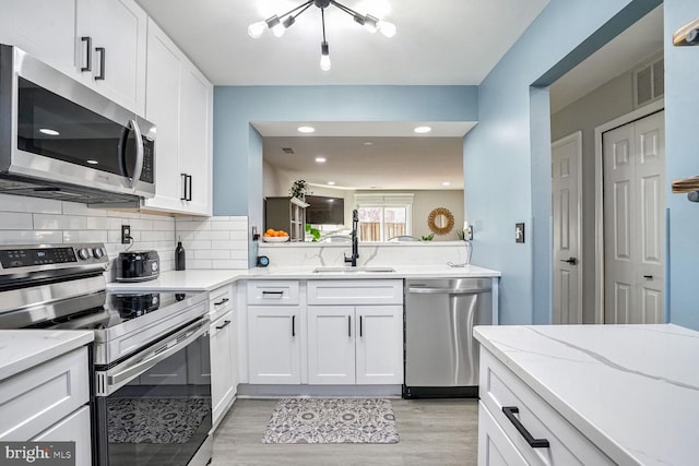 kitchen featuring appliances with stainless steel finishes, white cabinetry, decorative backsplash, sink, and light hardwood / wood-style flooring