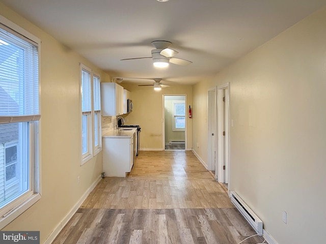 kitchen featuring light wood-type flooring, electric range oven, ceiling fan, a baseboard radiator, and white cabinetry