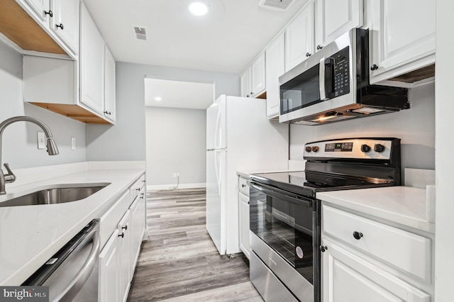 kitchen featuring white cabinets, sink, light stone countertops, light wood-type flooring, and stainless steel appliances