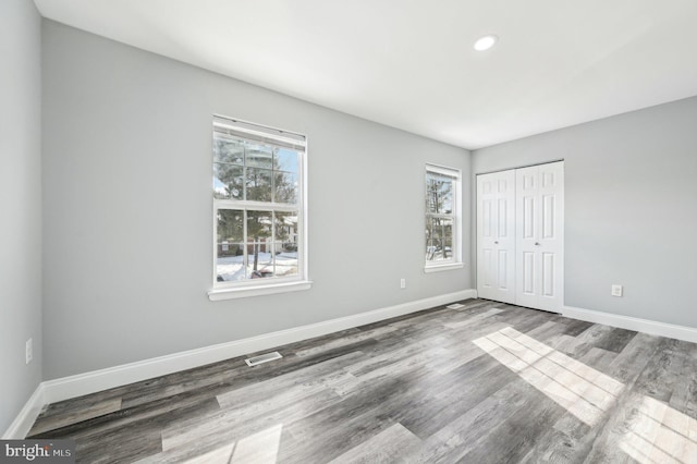 unfurnished bedroom featuring wood-type flooring, a closet, and multiple windows