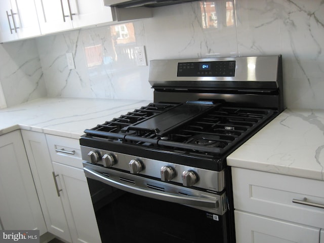 kitchen with white cabinets, decorative backsplash, stainless steel gas range oven, and light stone counters