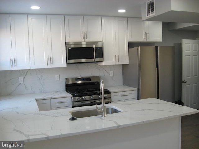 kitchen with white cabinets, decorative backsplash, light stone countertops, and appliances with stainless steel finishes