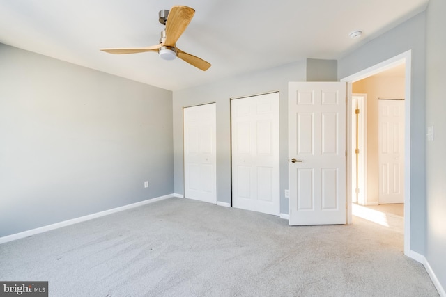 unfurnished bedroom with ceiling fan, light colored carpet, and two closets