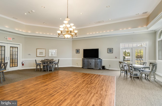 living room featuring a towering ceiling, a notable chandelier, a tray ceiling, crown molding, and french doors