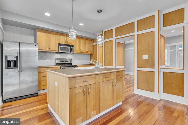 kitchen with hanging light fixtures, appliances with stainless steel finishes, a center island with sink, and light brown cabinetry