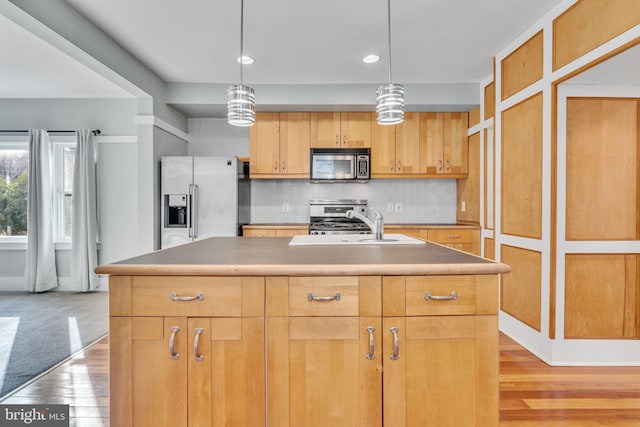 kitchen featuring sink, tasteful backsplash, an island with sink, stainless steel appliances, and light hardwood / wood-style floors