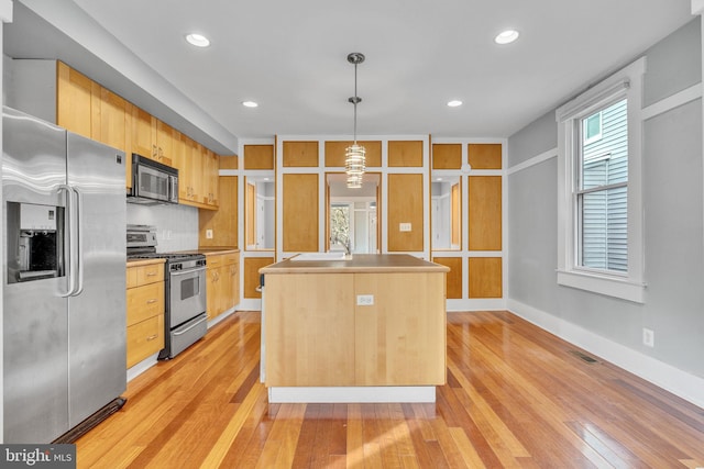 kitchen with light brown cabinets, light wood-type flooring, appliances with stainless steel finishes, an island with sink, and pendant lighting