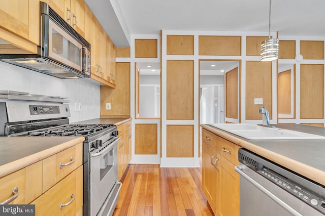 kitchen with sink, tasteful backsplash, decorative light fixtures, light wood-type flooring, and appliances with stainless steel finishes