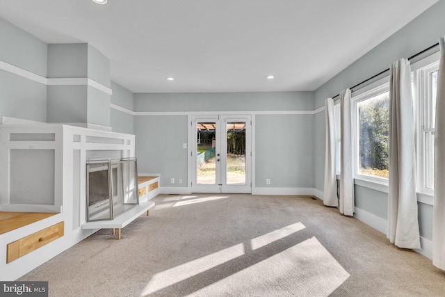 unfurnished living room featuring plenty of natural light, light colored carpet, and french doors