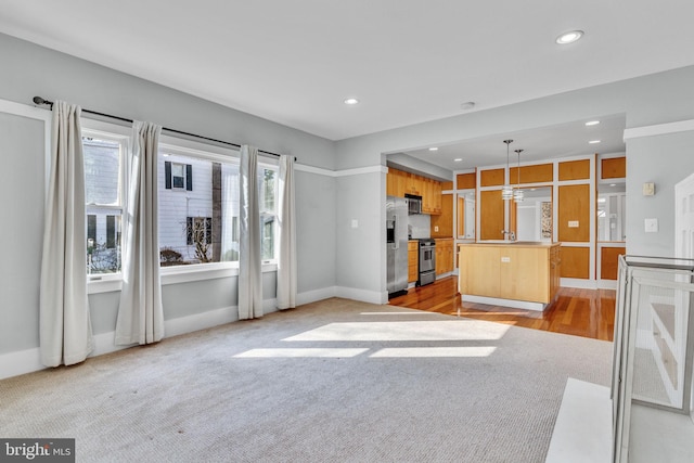 kitchen featuring stainless steel appliances, a kitchen island, light carpet, and hanging light fixtures