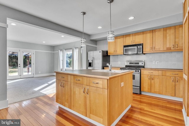 kitchen featuring appliances with stainless steel finishes, decorative light fixtures, tasteful backsplash, light hardwood / wood-style floors, and a center island with sink