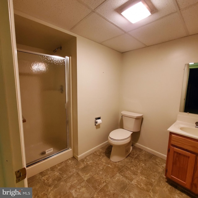 bathroom with a drop ceiling, vanity, a shower with door, and toilet