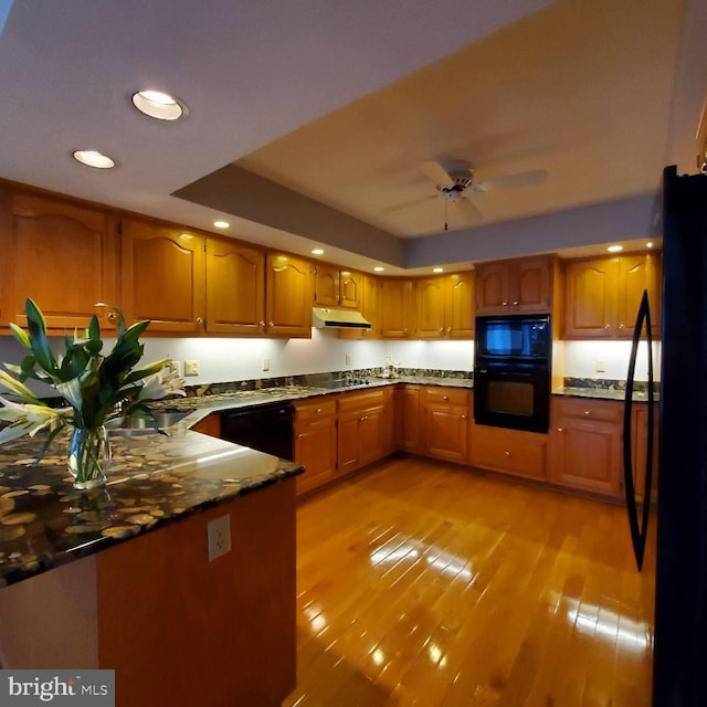 kitchen featuring light wood-type flooring, ceiling fan, dark stone counters, and black appliances