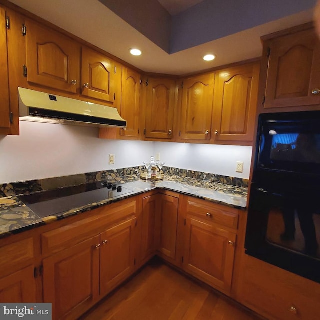 kitchen featuring black oven, stovetop, dark stone counters, and hardwood / wood-style flooring