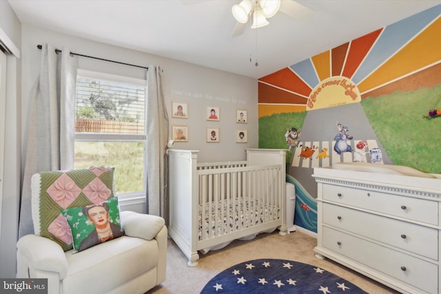 carpeted bedroom featuring a nursery area and ceiling fan