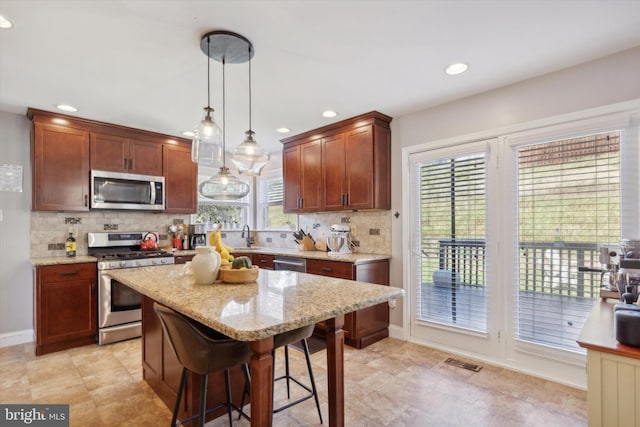 kitchen featuring a breakfast bar, appliances with stainless steel finishes, backsplash, a kitchen island, and decorative light fixtures