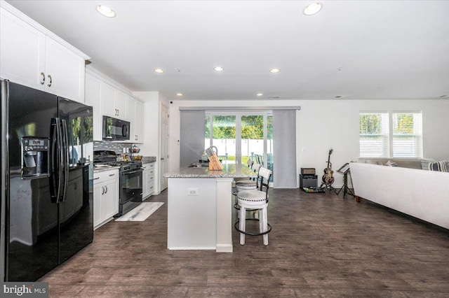 kitchen featuring a kitchen bar, light stone countertops, black appliances, white cabinets, and a center island