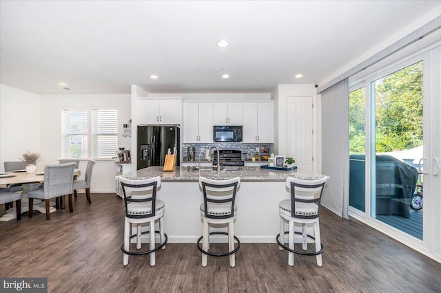 kitchen featuring a kitchen breakfast bar, an island with sink, white cabinetry, and black appliances