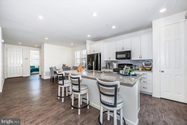 kitchen with white cabinetry, a kitchen breakfast bar, dark hardwood / wood-style floors, an island with sink, and black appliances