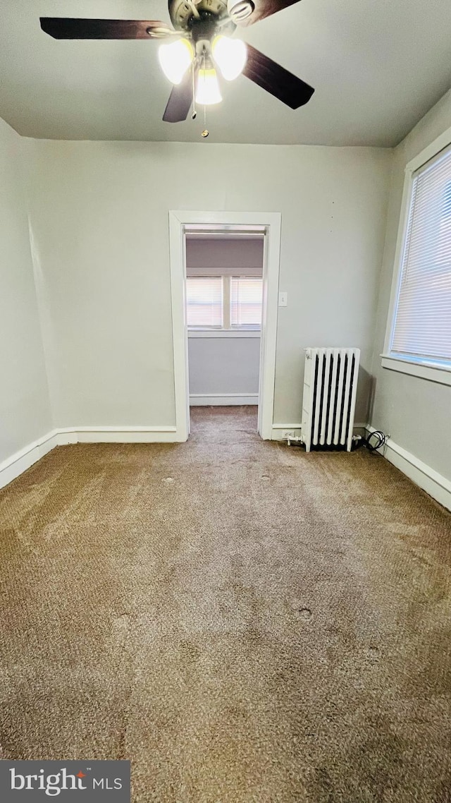 carpeted empty room featuring radiator and ceiling fan