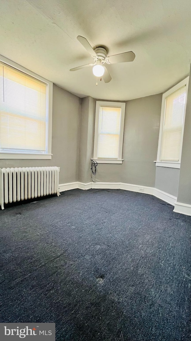 empty room featuring carpet, ceiling fan, plenty of natural light, and radiator