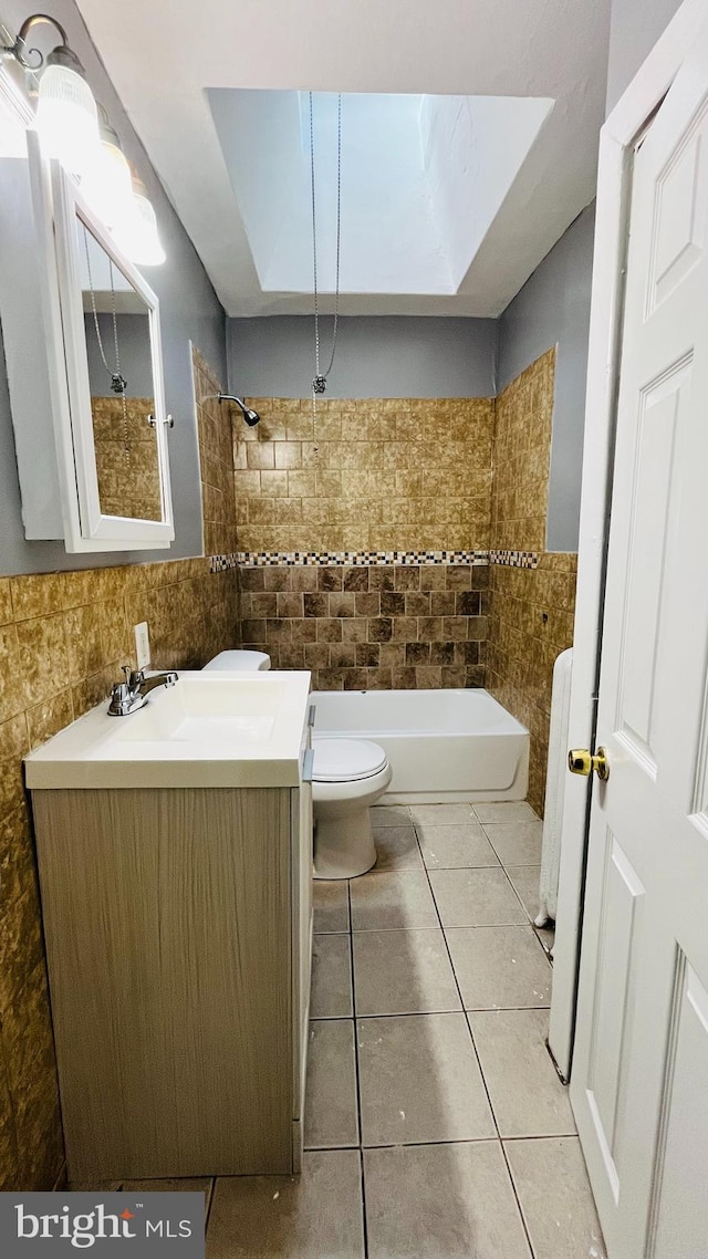 full bathroom with a skylight, washtub / shower combination, toilet, vanity, and tile walls