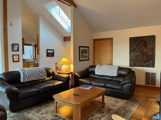 living room featuring a skylight, high vaulted ceiling, light hardwood / wood-style floors, and sink