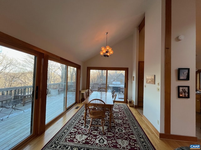 dining space with a notable chandelier, light hardwood / wood-style floors, and high vaulted ceiling