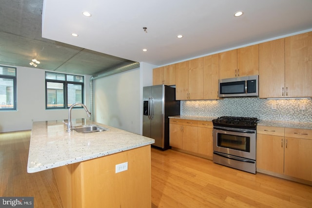 kitchen with light stone countertops, appliances with stainless steel finishes, a kitchen island with sink, sink, and light hardwood / wood-style flooring