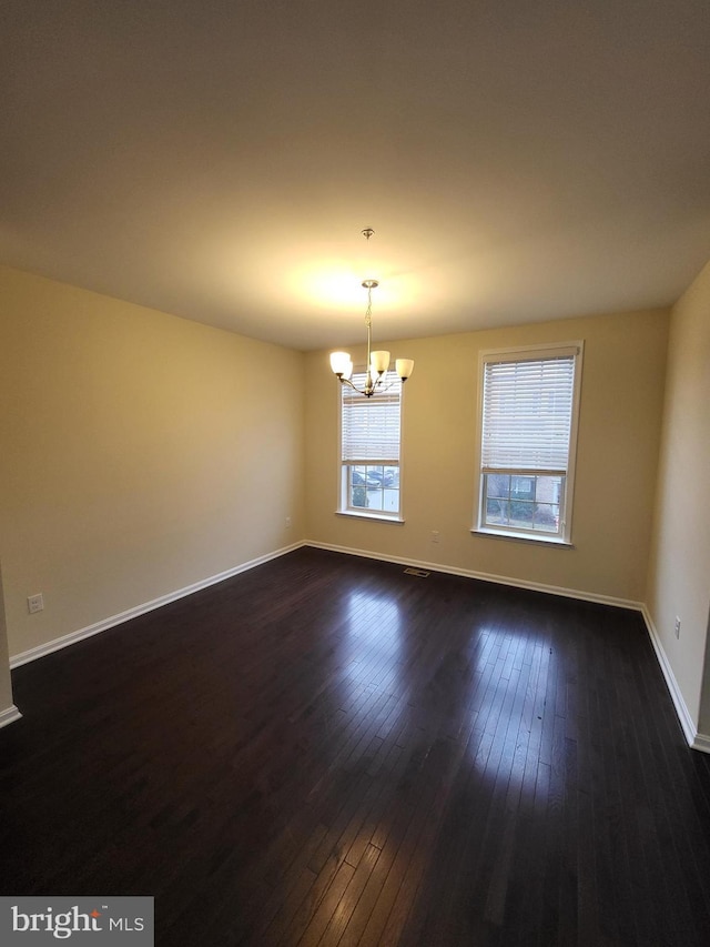 empty room featuring dark wood-type flooring and an inviting chandelier