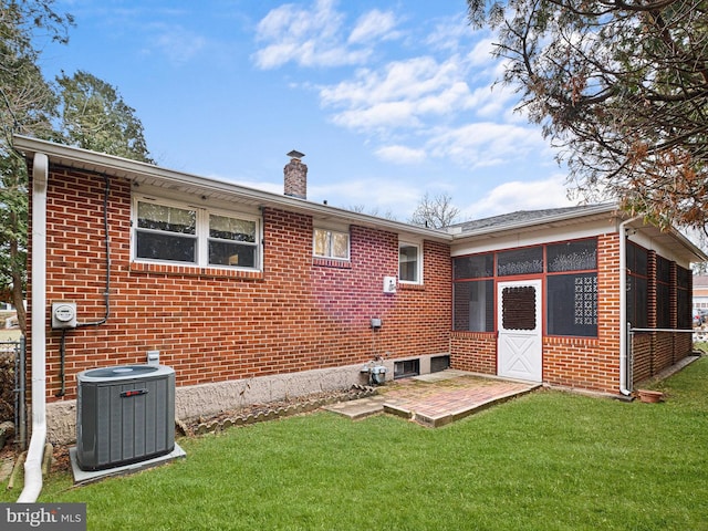 rear view of property with a lawn, a sunroom, and central AC unit