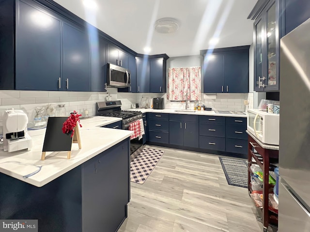 kitchen featuring blue cabinetry, sink, backsplash, light hardwood / wood-style floors, and appliances with stainless steel finishes