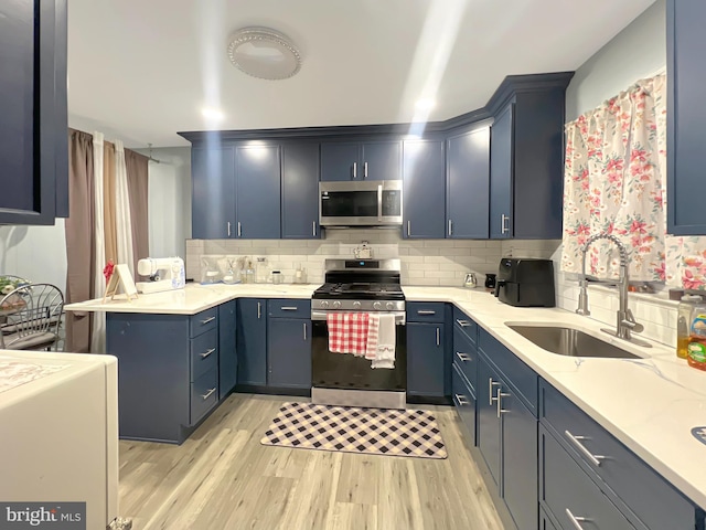 kitchen featuring appliances with stainless steel finishes, backsplash, sink, blue cabinetry, and light hardwood / wood-style flooring