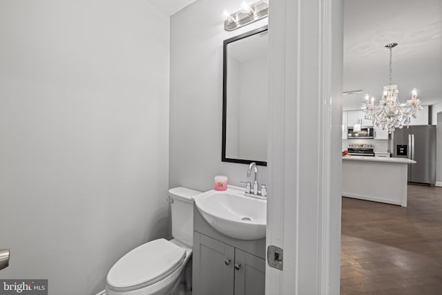 bathroom featuring hardwood / wood-style floors, vanity, an inviting chandelier, and toilet