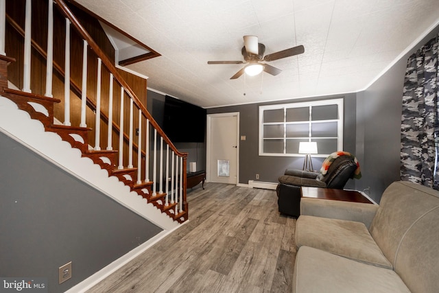 living area with wood finished floors, baseboards, baseboard heating, ceiling fan, and stairs