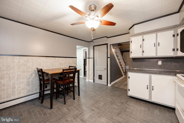 kitchen with a ceiling fan, dark countertops, ornamental molding, white cabinetry, and tile walls