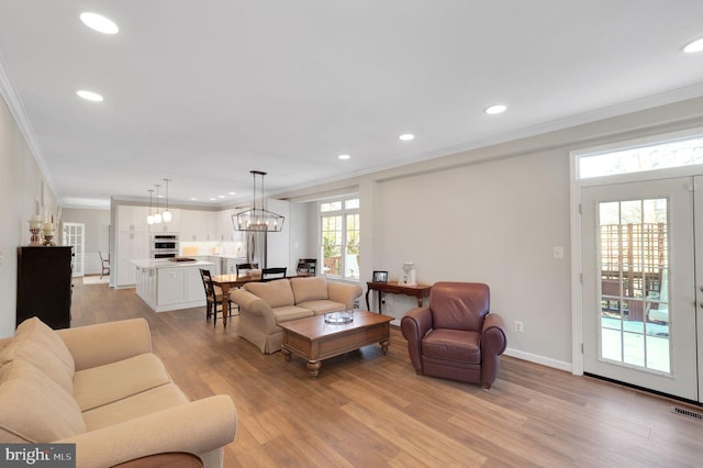 living room featuring crown molding, a wealth of natural light, a chandelier, and light hardwood / wood-style flooring