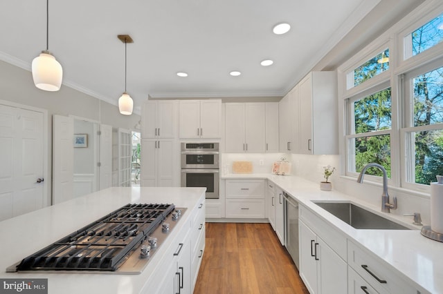 kitchen featuring stainless steel appliances, sink, white cabinets, and decorative light fixtures