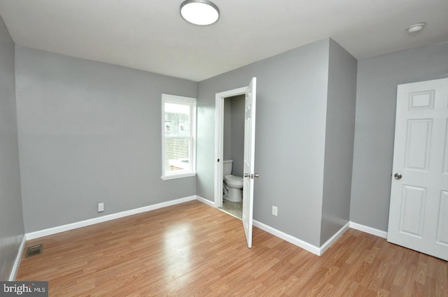 unfurnished bedroom with light wood-type flooring and connected bathroom