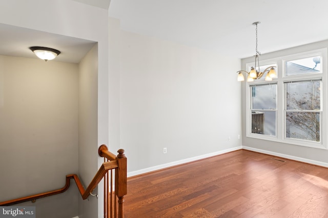 empty room with dark hardwood / wood-style flooring and an inviting chandelier