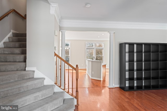 staircase with ornate columns, hardwood / wood-style flooring, and crown molding