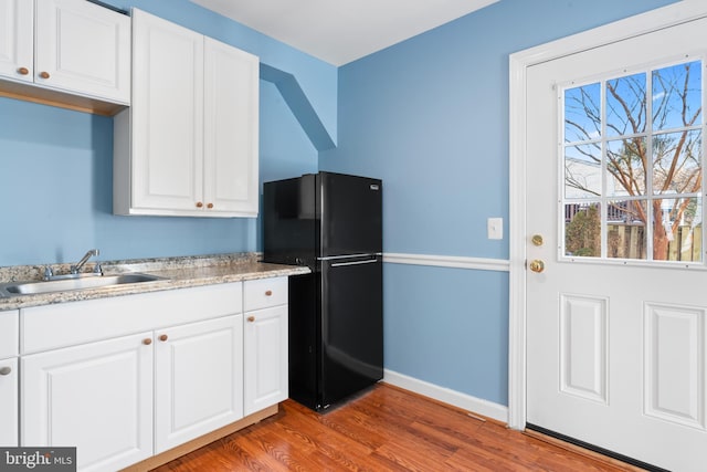 kitchen with white cabinets, hardwood / wood-style flooring, black refrigerator, and sink