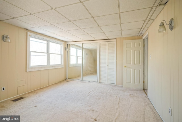 unfurnished bedroom featuring light carpet, a closet, a drop ceiling, and wood walls