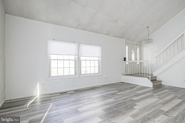 unfurnished living room with high vaulted ceiling, a textured ceiling, light hardwood / wood-style flooring, and a chandelier